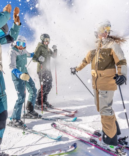 Skigruppe lacht und spielt im Schnee – aufgewirbelte Schneeflocken und Wintersonne sorgen für lebendige Dynamik. Symbolbild für Spaß und Erlebnis im Winterurlaub.